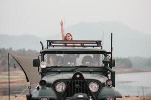 donna su un avventura onde allegramente a partire dal il tetto di un' fuori strada auto parcheggiata di un' tranquillo in riva al lago campeggio. foto