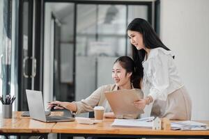 Due sorridente femmina colleghi collaborativamente Lavorando su un' progetto con un' il computer portatile e caffè nel un' luminosa ufficio spazio. foto