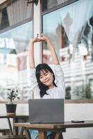 un' sereno giovane donna prende un' allungamento rompere a sua computer portatile, sorridente con chiuso occhi, godendo un' momento di rilassamento nel sua produttivo giorno. foto