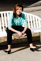 sorridente attraente asiatico americano donna seduta su panchina foto