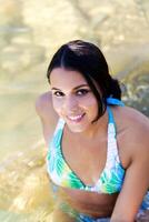 sorridente caucasico donna nel blu bikini seduta nel fiume foto