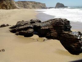 roccia e sabbia spiaggia con oceano onde e scogliere nel sfondo foto