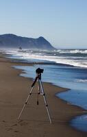 telecamera su tripode su spiaggia con oceano e colline foto