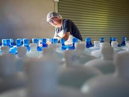 giovane uomo lavoratore o qualità ispettore nel abbigliamento da lavoro Lavorando nel controllo potabile acqua gallone nel bevanda acqua fabbrica prima spedizione.bere acqua affari,piccolo affari, negozio, magazzino foto