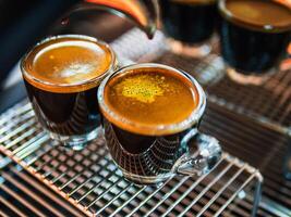 vicino su di caffè espresso tiro con caffè crema e professionale caffè macchina mentre preparazione Due espresso tiro bicchiere nel un' caffè negozio. foto