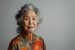 ai generato ritratto di anziano asiatico donna su un' solido grigio sfondo foto