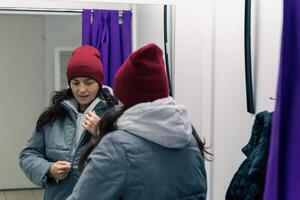 donna nel mezzo età provando su giacca e cappello nel adattamento camera a Raccogliere punto foto