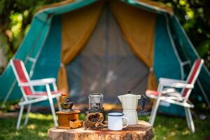 selettivo messa a fuoco di Vintage ▾ caffè impostato su il vecchio di legno tavolo nel davanti di il retrò cabina tenda, retrò sedie, gruppo di campeggio tende, e morbido messa a fuoco. foto