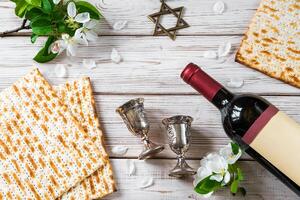 ebraico religioso vacanza di pasqua. bottiglia di vino, pane azzimo e fiori su bianca di legno sfondo. foto