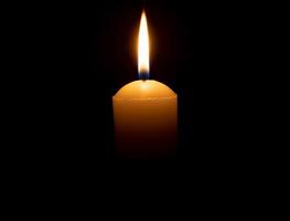 singolo ardente candela fiamma o leggero raggiante su grande bianca candela su nero o buio sfondo su tavolo nel Chiesa per Natale, funerale o memoriale servizio con copia spazio foto