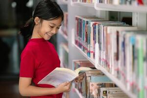 un' giovane ragazza è sorridente come lei sembra attraverso un' libro nel un' biblioteca foto