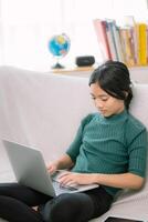 asiatico giovane ragazze fare compiti a casa su computer portatili su un' confortevole divano. foto