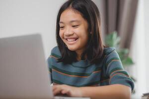 un' giovane ragazza è sorridente e utilizzando un' il computer portatile foto