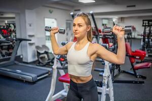 giovane donna detiene manubri nel sua mani e lavori su nel il Palestra l'esecuzione un esercizio foto