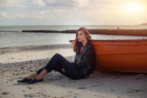un' ragazza lateralmente vicino un' rosso barca su il spiaggia di il mare foto