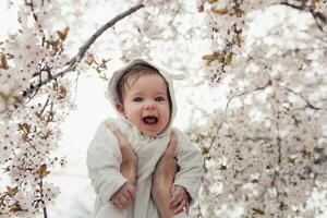 contento famiglia. madre mani lanci su bambino nel il fioritura Mela alberi, su soleggiato giorno nel il parco. foto