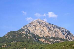 il montagna sbircia attraverso il alberi contro un' chiaro blu cielo con bianca nuvole. doyran stagno, antalya, tacchino. foto