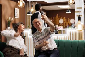 Visualizza a partire dal lusso Hotel atrio di pensionato anziano turisti fabbricazione Internet videochiamate. contento anziano coppia su loro luna di miele, collegamento con famiglia e amici attraverso cellula Telefono. foto