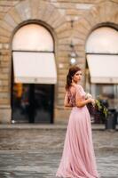 un' giovane bellissimo sposa sta a il centro di il vecchio città di Firenze nel Italia. sposa nel un' bellissimo rosa vestito con un' mazzo nel toscana.italia foto