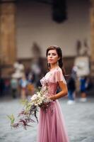 un' giovane bellissimo sposa sta a il centro di il vecchio città di Firenze nel Italia. sposa nel un' bellissimo rosa vestito con un' mazzo nel toscana.italia foto