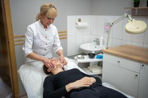 estetista medico asciugandosi del paziente viso con cotone pastiglie. ritratto di donna su pulizia viso procedura di donna cosmetologo nel bellezza clinica. bellezza industria concetto. foto