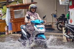 un' motociclista chi guidavo attraverso alluvione acque durante pesante pioggia nel un' Residenziale la zona, Indonesia, 8 dicembre 2023. foto