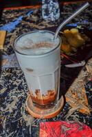 un' avvicinamento Visualizza di un ghiacciato caffè latte macchiato su un' strutturato di legno tavolo. foto