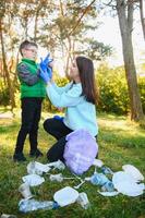 donna volontario e poco ragazzo raccolta su il plastica spazzatura e mettendo esso nel biodegradabile sacchetto della spazzatura all'aperto. ecologia, raccolta differenziata e protezione di natura concetto. ambientale protezione. foto