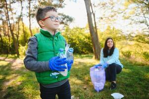 donna volontario e poco ragazzo raccolta su il plastica spazzatura e mettendo esso nel biodegradabile sacchetto della spazzatura all'aperto. ecologia, raccolta differenziata e protezione di natura concetto. ambientale protezione. foto