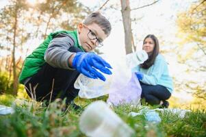 donna volontario e poco ragazzo raccolta su il plastica spazzatura e mettendo esso nel biodegradabile sacchetto della spazzatura all'aperto. ecologia, raccolta differenziata e protezione di natura concetto. ambientale protezione. foto