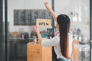 un' dedito bar proprietario si blocca un invitante 'Benvenuto Aperto cartello, segnalazione il inizio di il giorno nel sua accogliente caffè negozio, un emblema di piccolo attività commerciale ospitalità e prontezza. foto