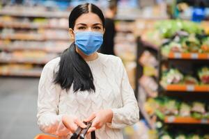 allarmato femmina indossa medico maschera contro coronavirus mentre drogheria shopping nel supermercato o negozio- Salute, sicurezza e pandemia concetto - giovane donna indossare protettivo maschera e accumulo cibo. foto