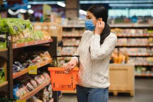 allarmato femmina indossa medico maschera contro coronavirus mentre drogheria shopping nel supermercato o negozio- Salute, sicurezza e pandemia concetto - giovane donna indossare protettivo maschera e accumulo cibo. foto