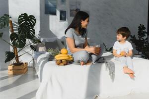 mamma con figlio nel pigiama mangiare frutta su letto. ritratto felice, sorridente, gioioso famiglia, madre e figlio avendo prima colazione nel letto, sorpresa su mamma giorno. positivo umano emozioni foto