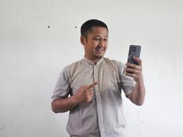 adulto asiatico uomo guardare e puntamento per il suo telefonino con stupito espressione foto