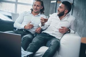 avvicinamento. due uomini d'affari seduti davanti al laptop che parlano dei loro piani e bevono whisky