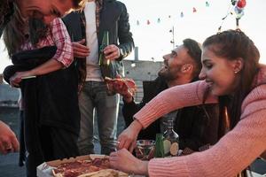 mangiare la pizza alla festa sul tetto. i buoni amici passano il fine settimana con del cibo e dell'alcol deliziosi foto