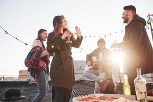 pizza in tavola. festa sul tetto con un po 'di alcol e suonare la chitarra. il sole dietro foto