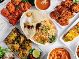 assortito famoso indiano e pakistano cibo tavolo verdura biryani, burro pollo, paneer pollo tikka boti kebab, lime, kali Mirchi, pomodoro salsa, rata, Roti, insalata, superiore Visualizza su grigio sfondo foto