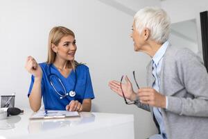 giovane donna medico o gp nel bianca medico uniforme consultare anziano femmina paziente nel privato Ospedale. femmina terapista parlare parlare con donna cliente su consultazione nel clinica. foto