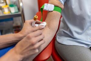 preparazione per sangue test con anziano donna di femmina medico medico uniforme su il tavolo nel bianca luminosa camera. infermiera trafigge il del paziente braccio vena con ago vuoto tubo. foto