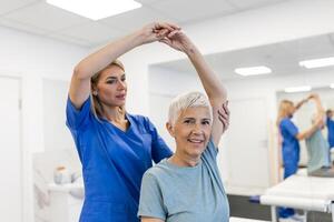 medico o fisioterapista Lavorando l'esame trattamento ferito braccio di anziano femmina paziente, allungamento e esercizio, fare il reinserimento terapia dolore nel clinica. foto