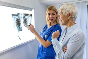 medico donna controllo raggi X film nel medico laboratorio a Ospedale, spiegando il risultati di scansione polmone su schermo per anziano paziente. foto