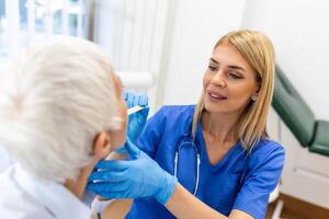 anziano paziente apertura sua bocca per il medico per Guarda nel sua gola. femmina medico l'esame dolorante gola di paziente nel clinica. otorinolaringoiatra esamina dolorante gola di paziente. foto