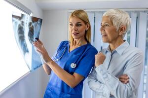 medico donna controllo raggi X film nel medico laboratorio a Ospedale, spiegando il risultati di scansione polmone su schermo per anziano paziente. foto