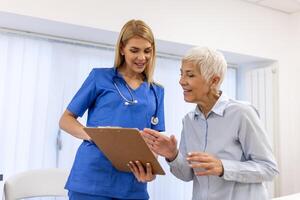 giovane femmina medico consulenza anziano vecchio paziente Riempimento modulo a consultazione. professionale medico uniforme parlando per maturo donna firma medico carta a appuntamento visitare nel clinica. foto