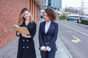 Due riuscito attività commerciale donne siamo parlando nel il città nel davanti di un' moderno costruzione. attività commerciale incontro su il strada. 2 femmina manager con superiore posizioni. foto