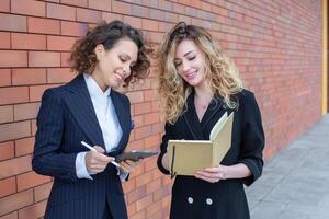 Due riuscito attività commerciale donne siamo parlando nel il città nel davanti di un' moderno costruzione. attività commerciale incontro su il strada. 2 femmina manager con superiore posizioni. foto