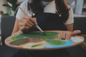 ritagliata Immagine di femmina artista in piedi nel davanti di un cavalletto e immersione spazzola in colore tavolozza foto