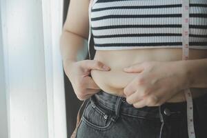 donne corpo Grasso gonfiarsi. obeso donna mano Tenere eccessivo pancia Grasso. dieta stile di vita concetto per ridurre pancia e forma su salutare stomaco muscolo. foto